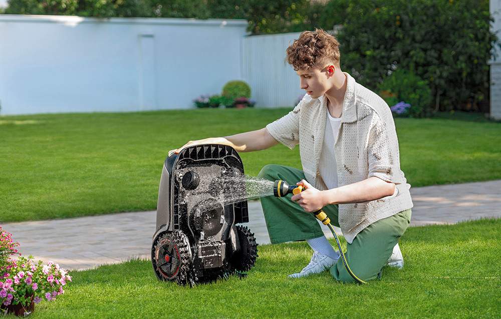 Muž myje robotickou sekačku na zahradě.